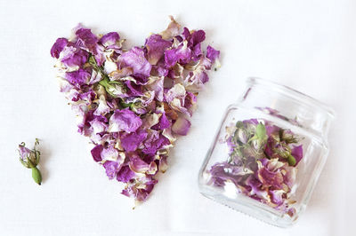 High angle view of rose hip petals in heart shape by jar on white background