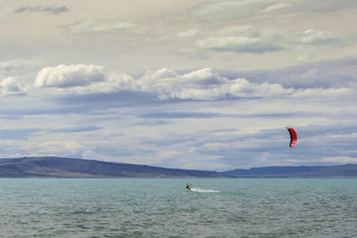 Scenic view of person surfing in water against cloudy sky