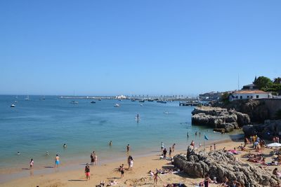 People on beach against clear blue sky