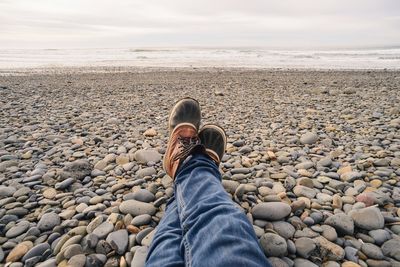 Low section of man sitting on pebbles at beach