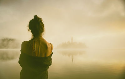 Woman in gray coat watching a sunrise among the fog on the shores of lake bled, slovenia v