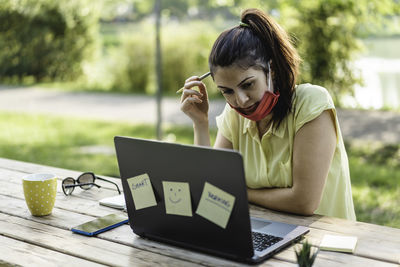 Thoughtful woman wearing mask with laptop sitting at park