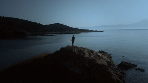 Man standing on rock formation in sea against sky