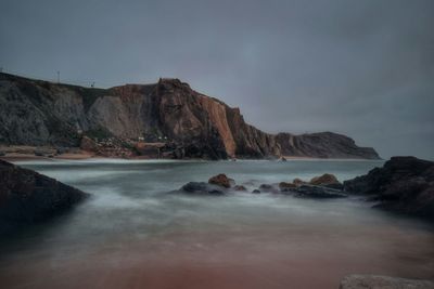 Scenic view of mountain at sea shore against sky during sunset