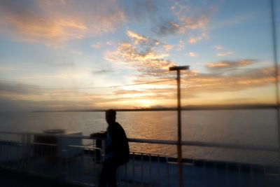 Silhouette man looking at sea against sky during sunset