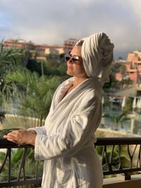 Woman in sunglasses and bathrobe watching the sunset from the hotel balcony