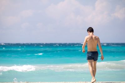 Shirtless man walking at beach against sky