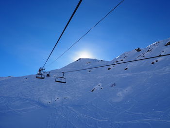 Low angle view of ski lift over snowcapped mountains against blue sky