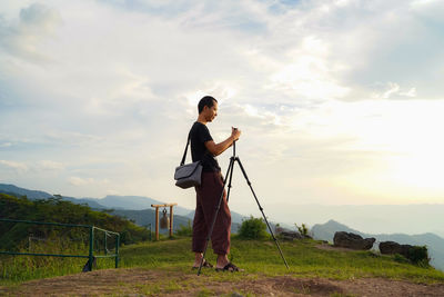 Side view of man photographing while standing on land against sky