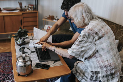 Senior woman discussing over laptop while sitting with male caregiver at home