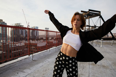 Young woman with arms raised standing in city against sky