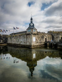 Reflection of buildings in lake against cloudy sky