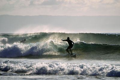 Silhouette man surfing in sea against sky