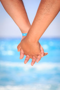 Close-up of women holding hands against sea and sky