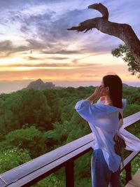 Side view of young woman looking away while standing against sky during sunset