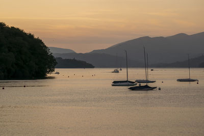 Sailboats moored on sea against sky during sunset