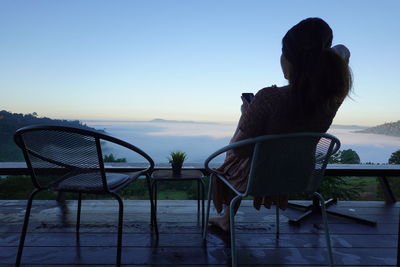 Rear view of woman sitting on bench looking at sunset