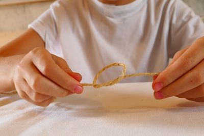 Midsection of person tying knot with string on table