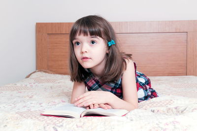 Young woman reading book while sitting on bed at home