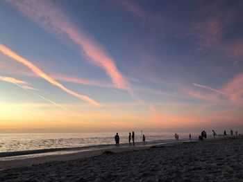 Silhouette people on beach against sky during sunset