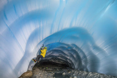 Side view of mountaineer ice climbing in glacial cave.