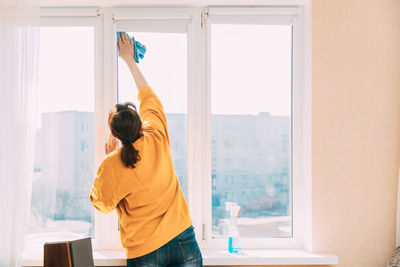 Rear view of woman cleaning window at home