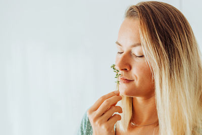 Close up of a woman smelling thyme, aromatic herbs on plain background