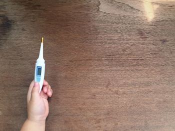 Cropped hand of child holding thermometer over table