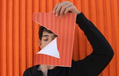 Boy holding torn paper against orange wall