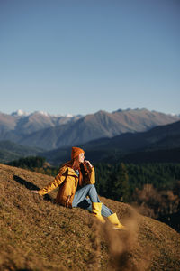 Side view of woman sitting on mountain against sky