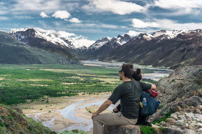 Rear view of woman sitting on rock against mountains