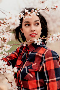 Young woman looking away while standing by cherry tree