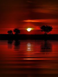 Silhouette trees by swimming pool against romantic sky at sunset