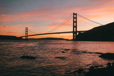 Suspension bridge over sea against sky during sunset