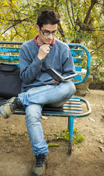 Full length of man reading book while relaxing on bench at park