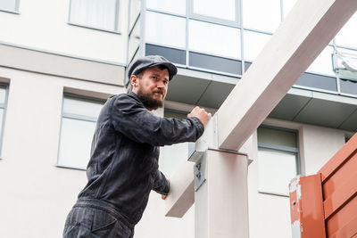 A young man with a beard builder in a construction black uniform, a gray cap builds a house 