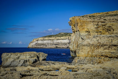 Rock formations by sea against blue sky