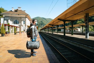 People with mask on railroad station against mountains and sky