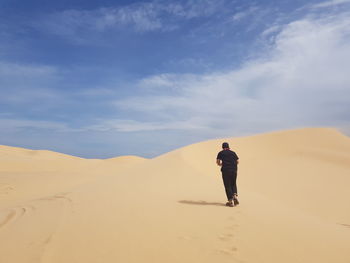 Rear view of man walking on sand dune against sky