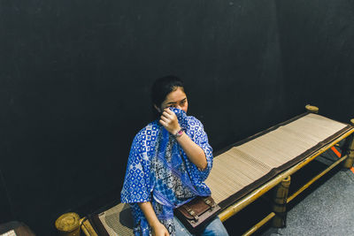 Portrait of woman covering face with scarf while sitting on bench