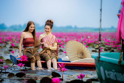 Woman sitting by pink flower against sky