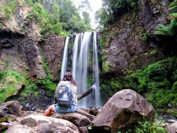 Woman sitting on rock against waterfall in forest