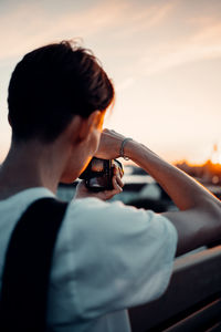 Portrait of man holding camera against sky during sunset