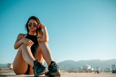 Young woman wearing sunglasses sitting on mountain against sky