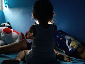 Rear view of women sitting on bed at home