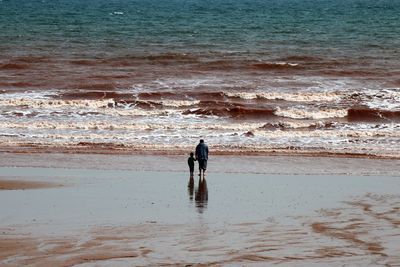 Father with son standing at beach on sunny day