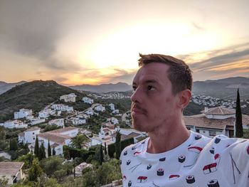 Portrait of young man with townscape against sky during sunset