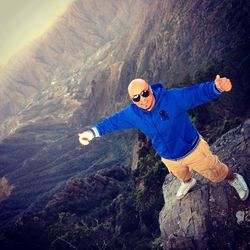 High angle portrait of man with arms outstretched gesturing thumbs up on mountain