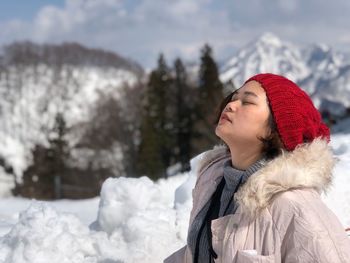 Woman with eyes closed against snow covered trees during winter