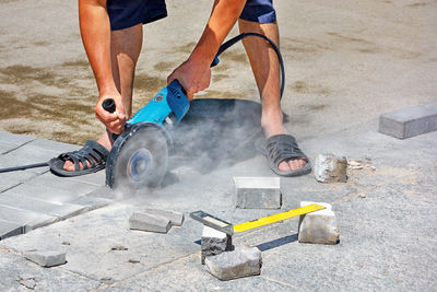 A worker cuts paving slabs with a grinder with a diamond cutting disc on a summer afternoon.